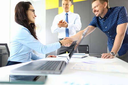 Man and woman businessmen shake hands at table with laptop in office portraitの写真素材
