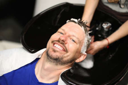 Young man washes hair with shampoo in sink in beauty salonの写真素材