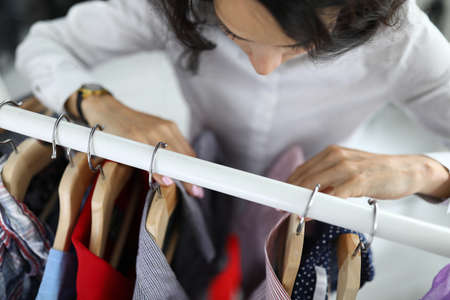 Young woman chooses shirt on hangers in wardrobe at home closeupの写真素材