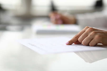 Female hand points finger at line in document at table in office closeupの写真素材