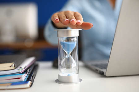 Woman holds her hand over hourglass at workplace in office closeupの写真素材
