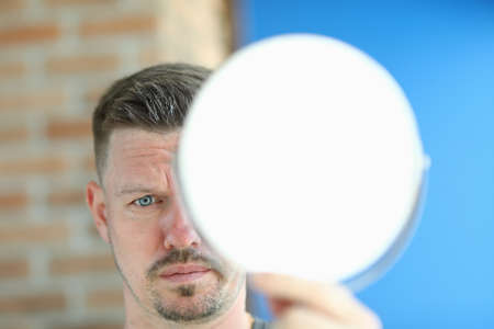 Young man with remnants of hair paste on head stands with mirror in hands portraitの写真素材