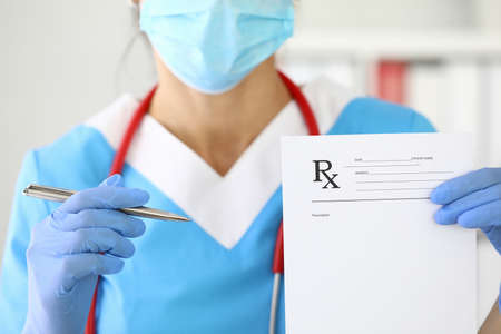 Doctor in protective mask on his face holds ballpoint pen and recipe closeupvの写真素材