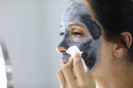 Young woman washes away black clay mask from face portraitの写真素材