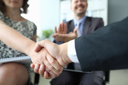 Handshake of man and woman closeup and cheering businessman in background in officeの写真素材