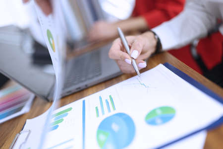 Womans hand holds ballpoint pen over documents with graphs and diagrams in office closeupの写真素材