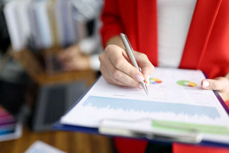 Business woman in red jacket holds clipboard with documents and pen closeupの写真素材