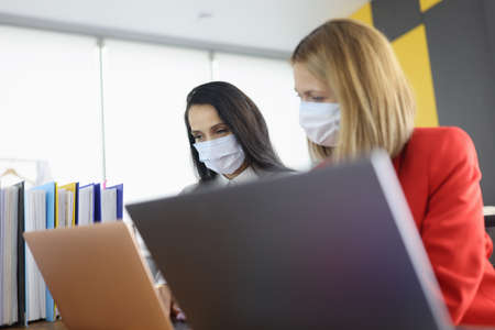 Two business women colleagues are looking at laptop on desktop in officeの写真素材