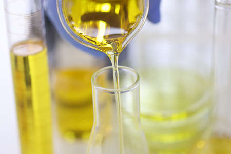 Scientists hand in rubber glove pours yellow liquid into glass test tube in chemical laboratory closeupの写真素材