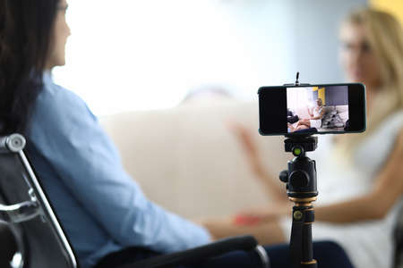 Two women sit and communicate conversation is recorded on smartphone.の写真素材