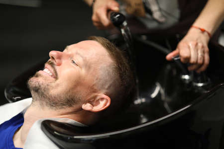 Master washes mans head in sink in hairdresser.の写真素材