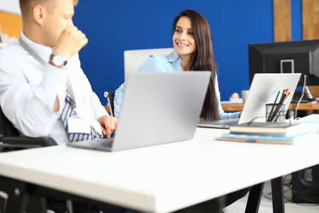Man and woman in office are sitting at their desk, smiling and looking at each other.の写真素材