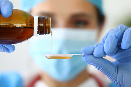 Doctor holds syrup and pours it into spoonの写真素材