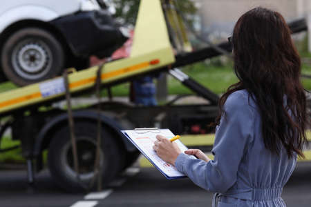 Woman insurance agent prepares documents for car that is taken away by tow truckの写真素材