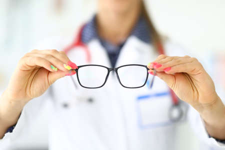 Ophthalmologist with stethoscope around neck holds glasses for vision in clinic closeupの写真素材
