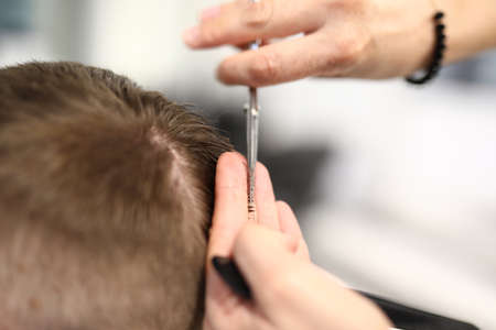 Hands of hairdresser with scissors make short haircut to man in beauty salon closeup