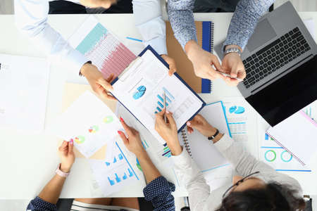 Group of business people men and women sit at table in office with papers, laptop and phone top viewの写真素材