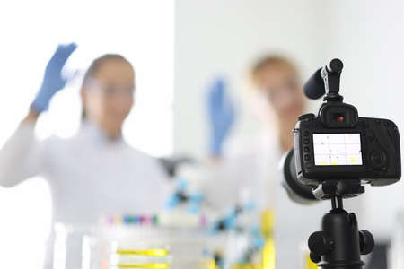 Camera captures female chemist bloggers who are waving in chemical laboratory closeup