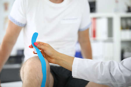 Doctors hands glue kinesio tape on patients knee.の写真素材