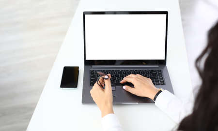 Woman has laptop on table next to smartphone and glasses.の写真素材
