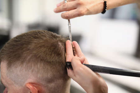 Masters male head holds comb in his hands and cuts his hair with scissors.の写真素材