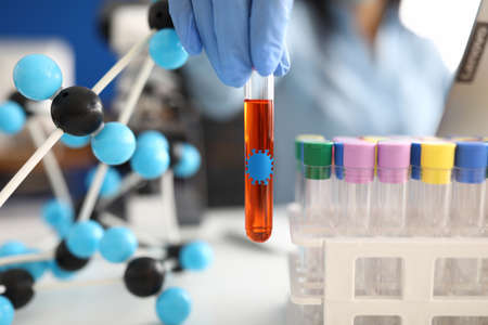 Hand in glove holds test tube with liquid on background of molecules and test tubesの写真素材