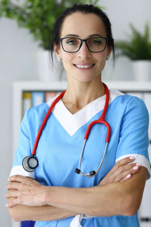 Woman medical worker in glasses and stethoscope stands with folded arms on her chestの写真素材