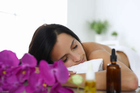 Woman with closed eyes lies on massage table in spa salonの写真素材