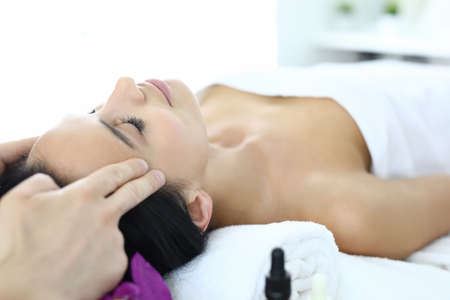 Woman lies on massage table with her eyes closed masseur does an acupressure face massageの写真素材