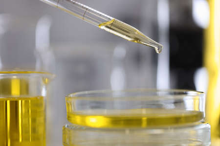 Yellow oil drips from test tube dispenser into the glass container.の写真素材