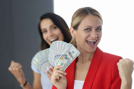 Two happy women are holding fan of one hundred dollar billsの写真素材
