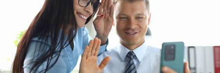 Business man and woman are looking at phone screen and waving hands in officeの写真素材