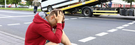 Minivan driver sits on side of road and holds his head during evacuation of his vehicleの写真素材