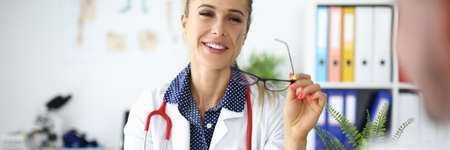 Smiling female doctor with glasses and stethoscope communicates with colleague with tablet in hand in clinicの写真素材