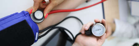 Cardiologist with red stethoscope measures blood pressure of patient in clinic closeupの写真素材