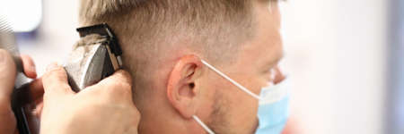Young man wearing protective face mask gets haircut with clipper in hairdresserの写真素材