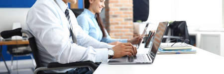 Young smiling man in wheelchair works at laptop in office with woman colleagueの写真素材