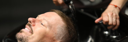 Master washes mans head in sink in hairdresser.の写真素材