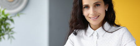 Businesswoman at table in office smiles and holds magnifying glassの写真素材