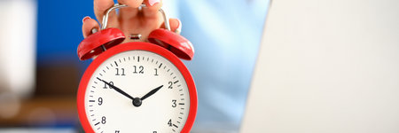 Womans hand lies on red alarm clock next to laptop.の写真素材