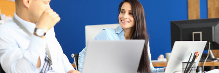 Man and woman in office are sitting at their desk, smiling and looking at each other.の写真素材