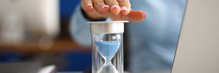 Woman holds her hand over hourglass at workplace in office closeupの写真素材