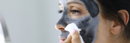 Young woman washes away black clay mask from face portraitの写真素材