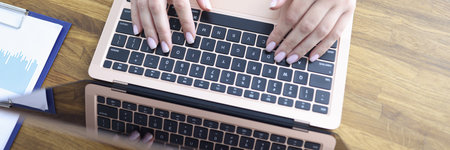 Female hands are typing on laptop keyboard at table in office closeup
