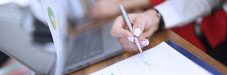 Womans hand holds ballpoint pen over documents with graphs and diagrams in office closeupの写真素材