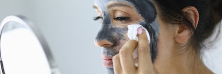Woman looks in mirror and rinses off an anti-aging face mask with cotton pad.の写真素材