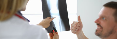Doctor woman holds an x-ray of leg beside the patient he smiles and shows thumbs upの写真素材