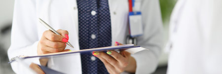 Silhouettes of two doctors in white coats one holding clipboard with pen, the second tablet.の写真素材