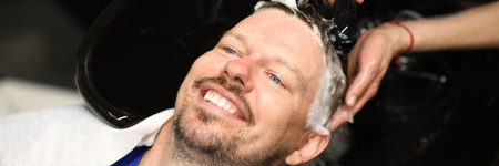 Portrait of smiling man who is being washed with shampoo in salon by master.の写真素材