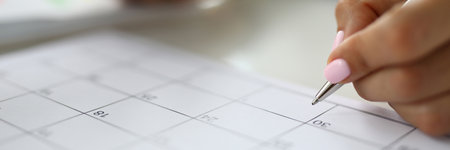 Womans hand holds pen and marks calendar.の写真素材